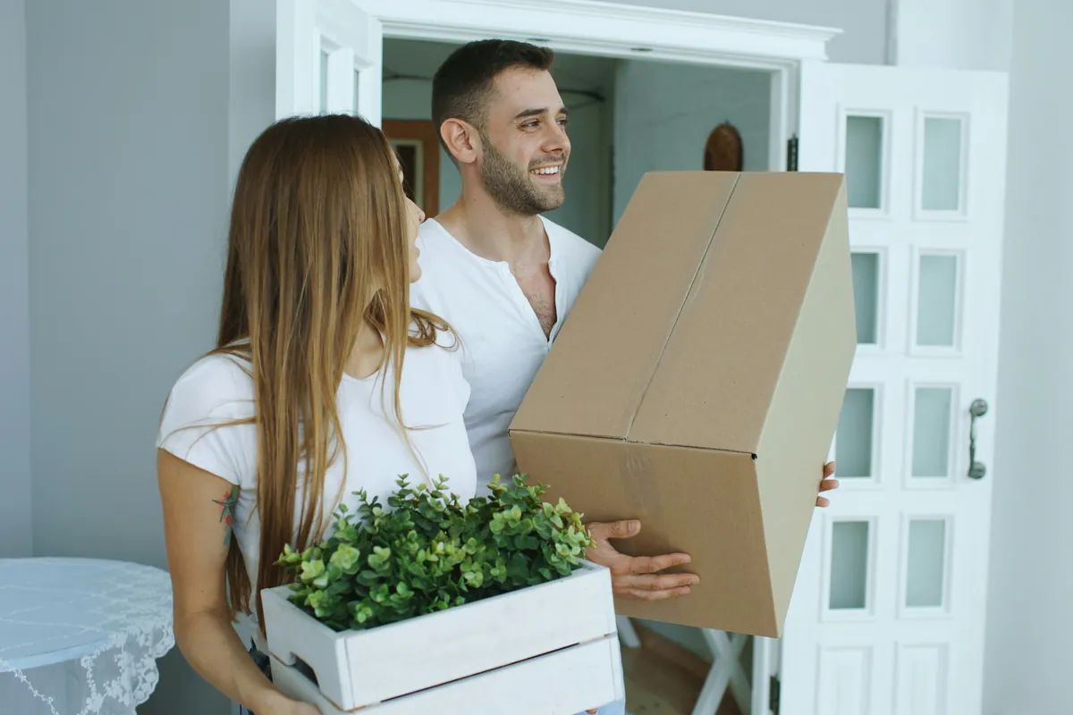 Couple carrying moving boxes into a new home