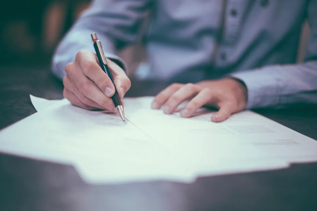 Close-up of a hand signing sale documents with a pen